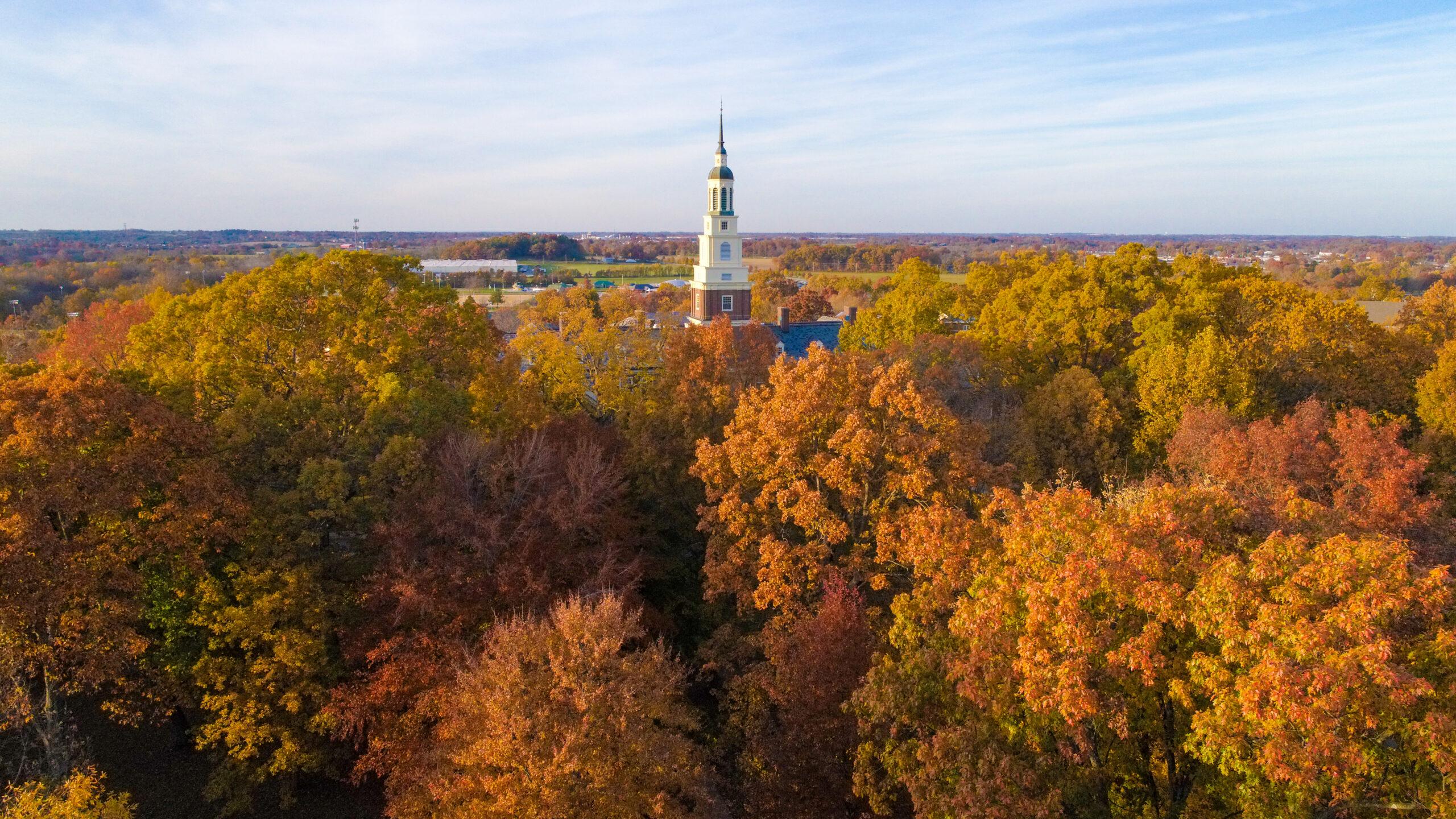 Draper Building rising above colorful autumn trees on campus.
